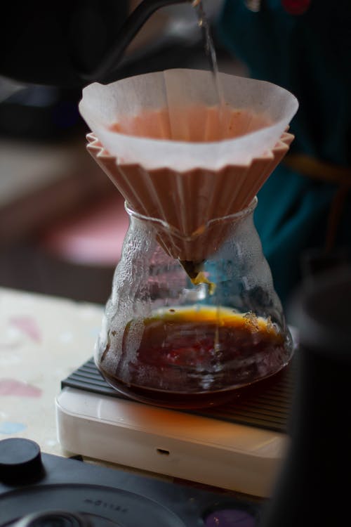 Hot water flowing into pour over filter placed on glass chemex for coffee brewing in modern kitchen