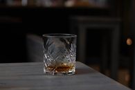 Cut glass with aromatic cognac on bottom placed on wooden table in dark living room