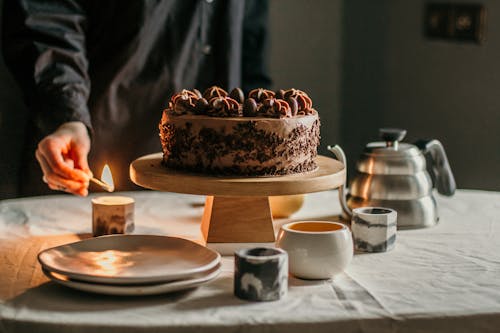 Person lighting candle placed near chocolate cake