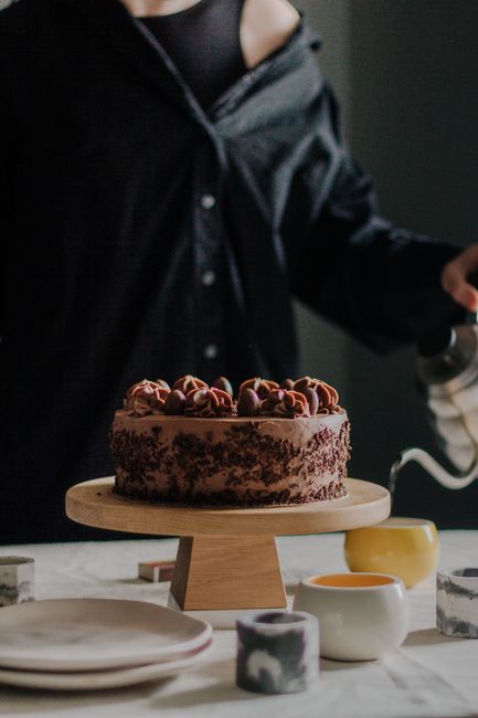 Crop anonymous female pouring hot tea into teapot during teatime with chocolate cake decorated with sweet cream