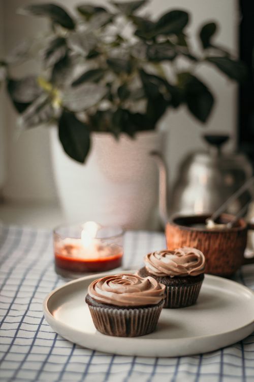 Free Tasty sweet homemade cupcakes with cream topping placed near burning candle and tea against potted plant Stock Photo