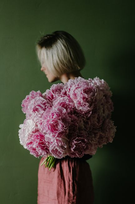 Side view of female standing with lush bouquet of peonies against green wall