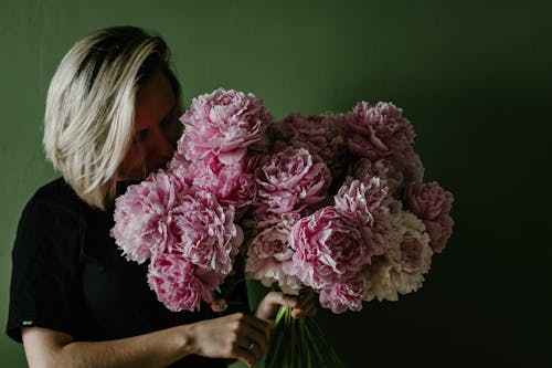 Free Female with dyed hair smelling bouquet of fragrant pink blooming peonies against green background Stock Photo