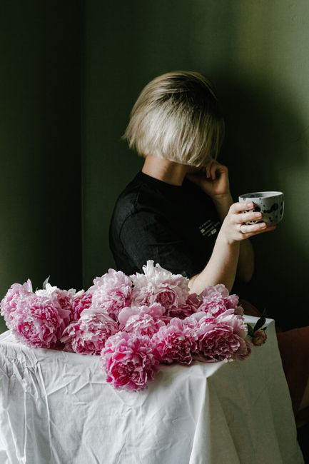 Side view of female florist with cup of hot drink sitting at table with peonies