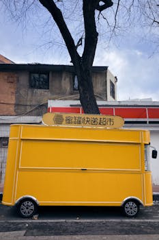 Vibrant yellow food truck parked on a street in Qingdao, China, on a clear day.