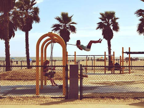 Kids enjoying a swing set by palm trees at Venice Beach, Los Angeles, California.