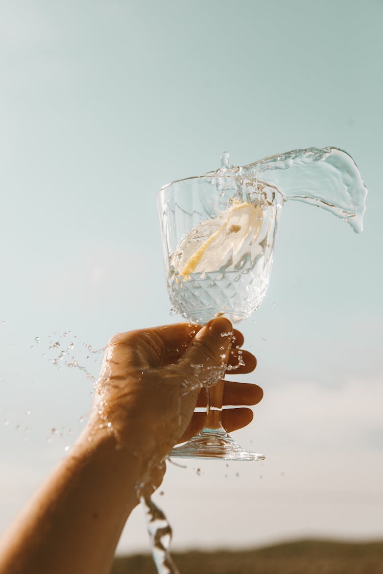 Hand Of A Person Spilling Lemon Water From A Wine Glass