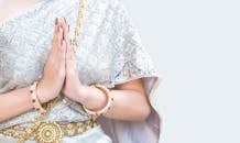 特写镜头中，一名女子身穿传统银色服装，戴着金色珠宝，双手合十，做出礼貌的手势