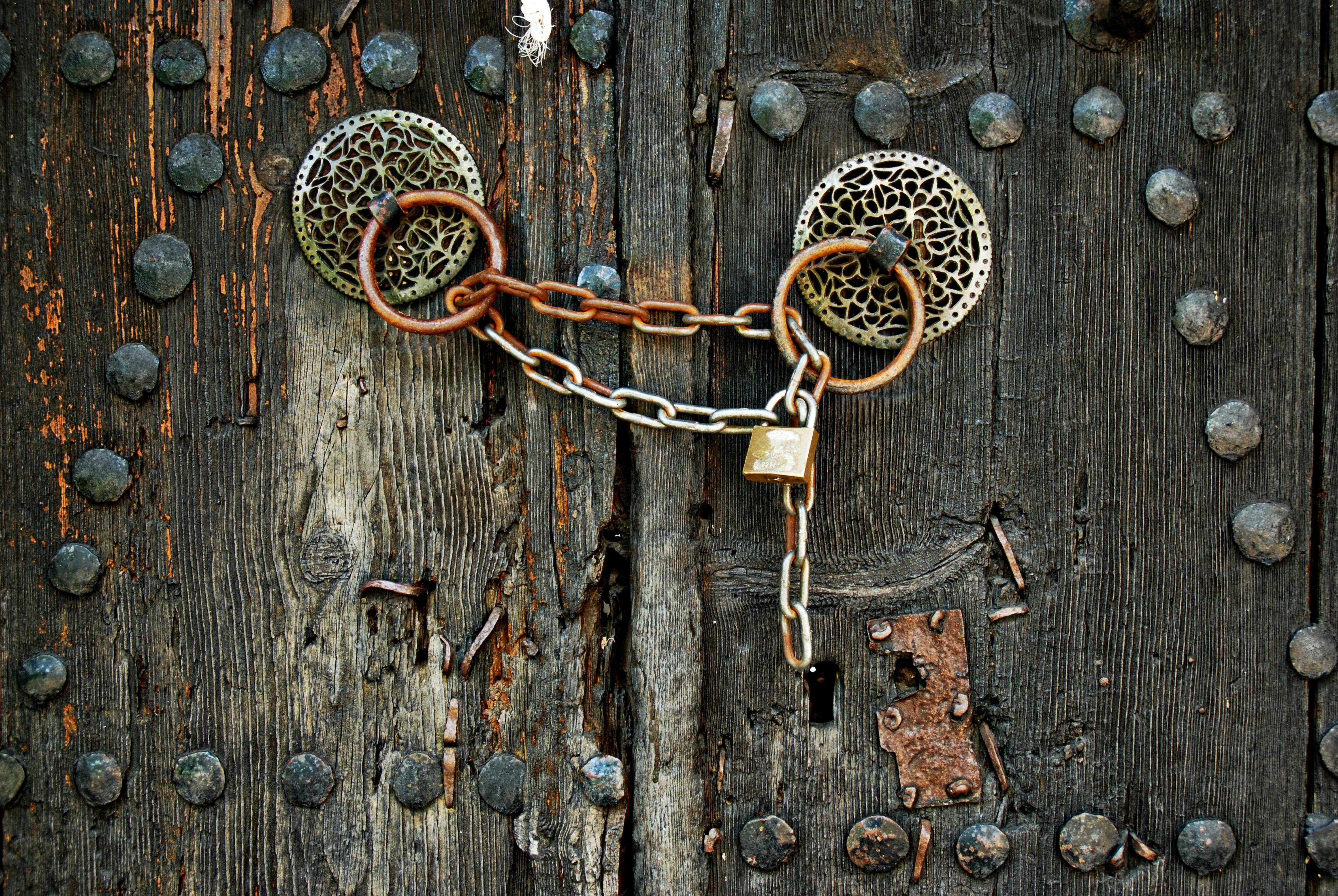 An old wooden door in Monodendri, Greece, featuring vintage metalwork and a padlock.