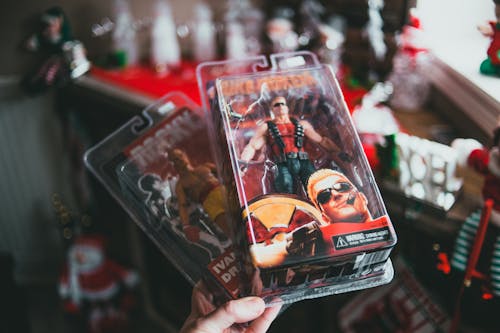 High angle of crop faceless person demonstrating packed toys of strong comic characters in souvenir shop during Christmas holidays