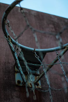 Close-up of a rusty basketball hoop with a metal chain net on a weathered backboard outdoors.