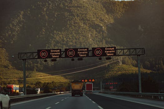 Highway with speed limit signs against a mountainous backdrop and low traffic.