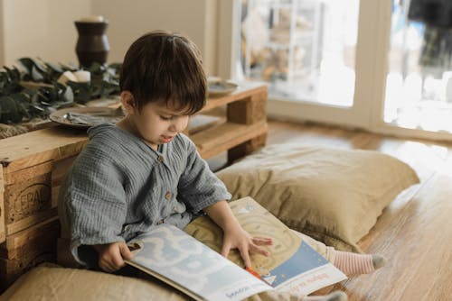 A Young Boy Sitting Near the Wooden Table while Holding a Book