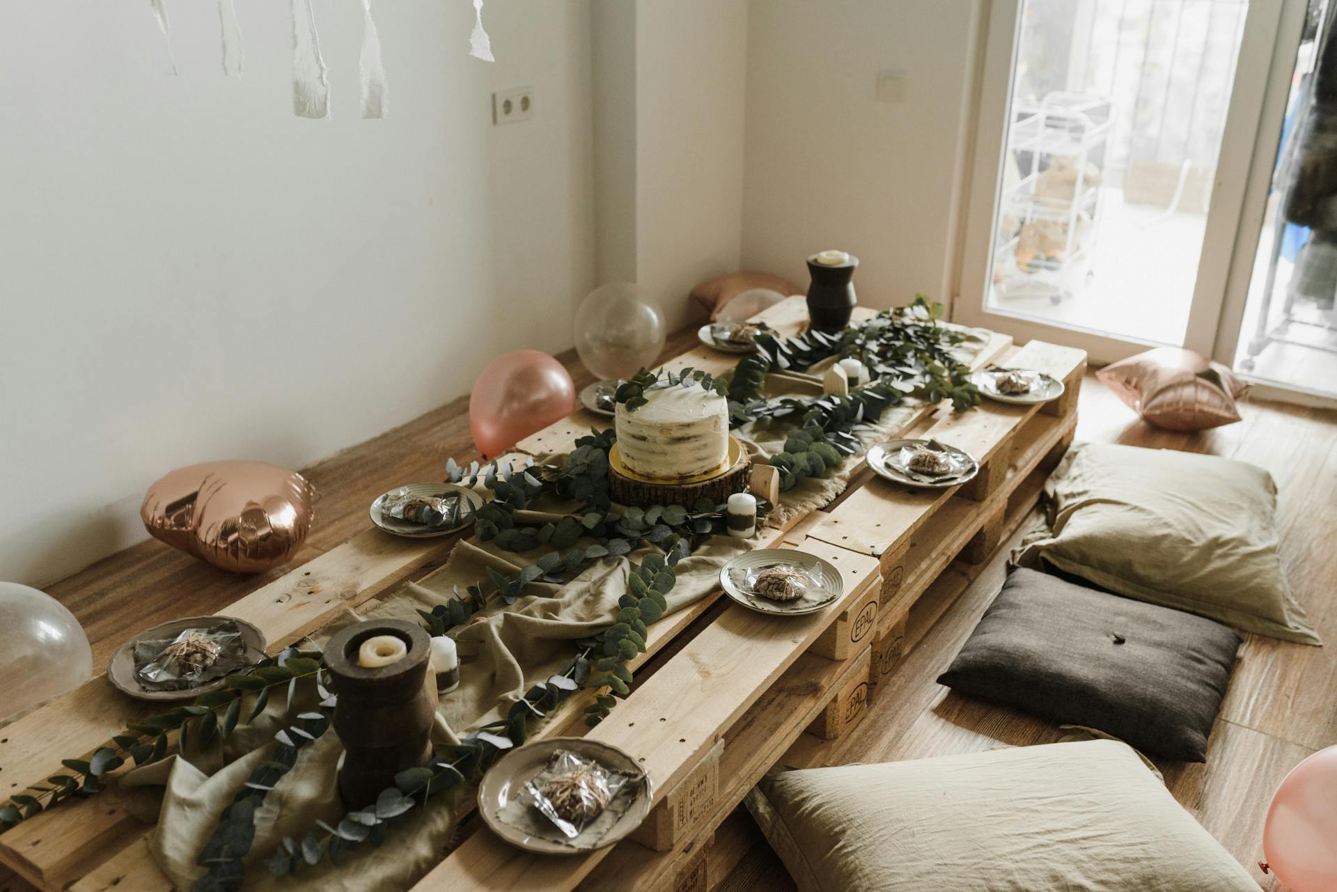 Rustic birthday setup featuring a wooden pallet table, cake, and decorations indoors.