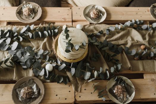 Vintage-style cake setup with eucalyptus on wooden tabletop.