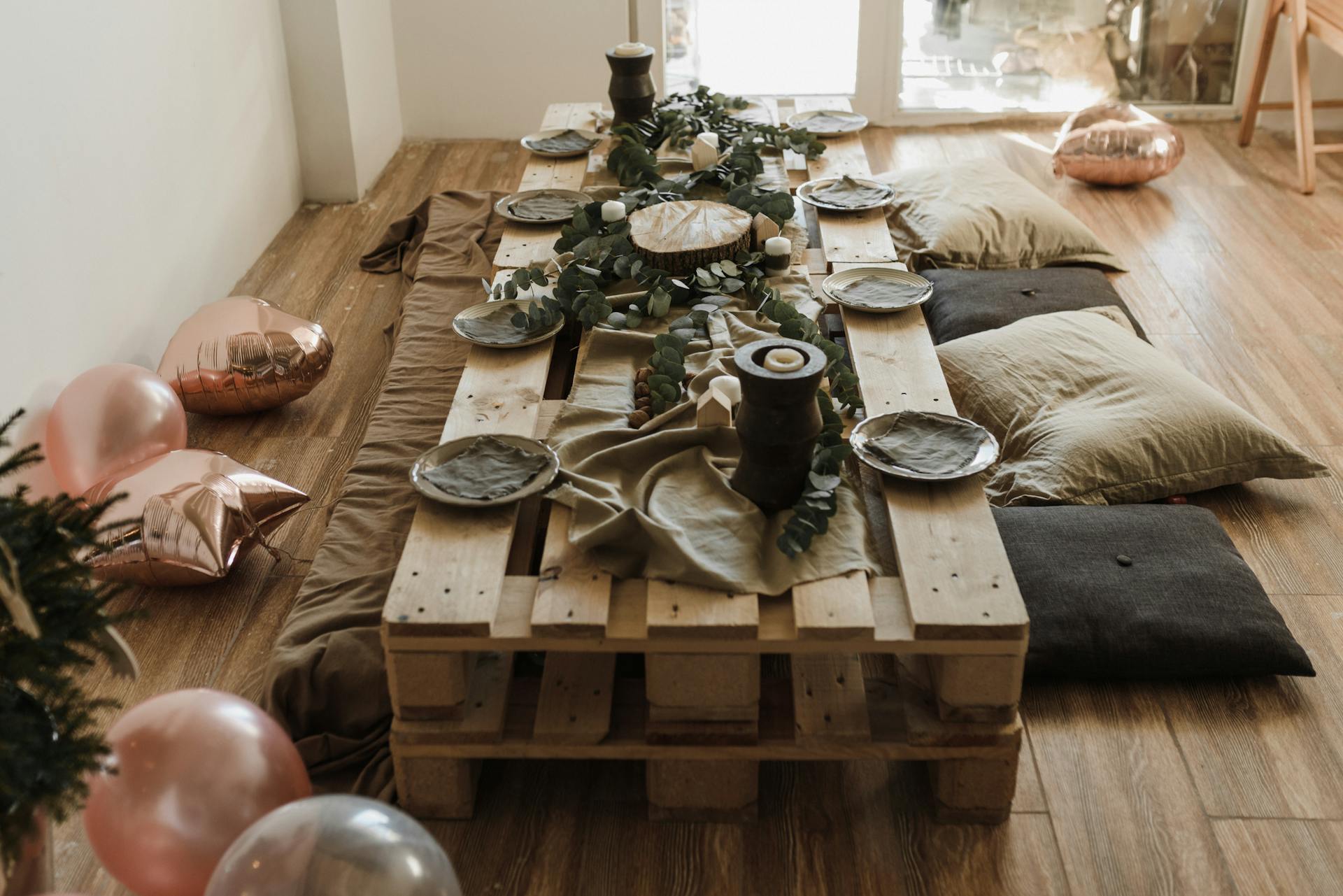 A cozy indoor party setup featuring a wooden pallet table, decorations, and casual seating.