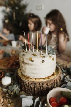 A rustic birthday cake with candles and children celebrating in the background.