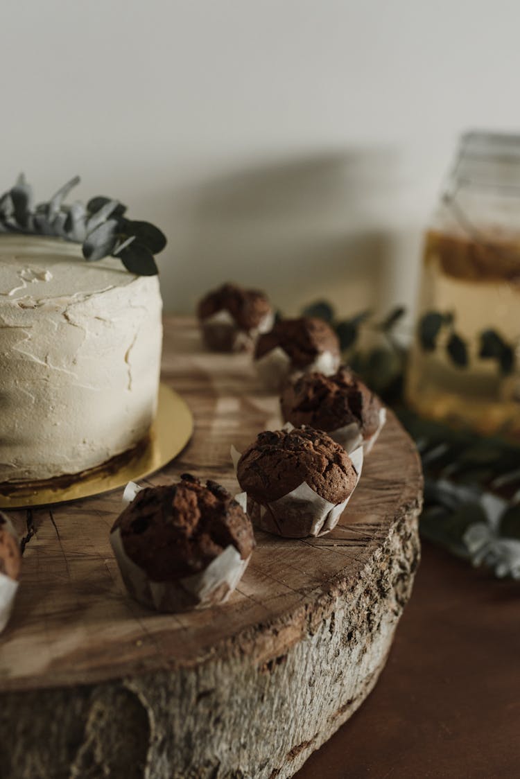 Close-up Of A Cake With Frosting And Chocolate Cupcakes Standing On A Wooden Surface