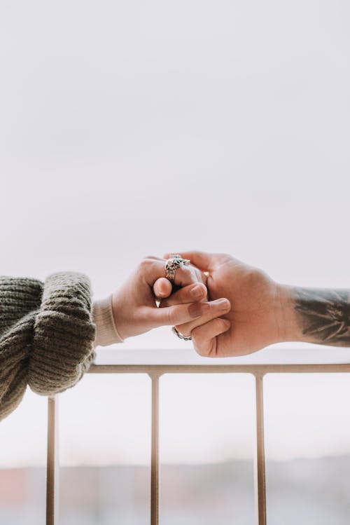Free Crop unrecognizable tattooed man and woman in warm sweater holding hands on balcony on cloudy day Stock Photo
