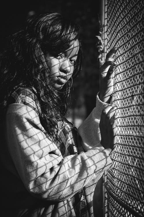 Серая фотография женщины, стоящей против решетчатой решетки