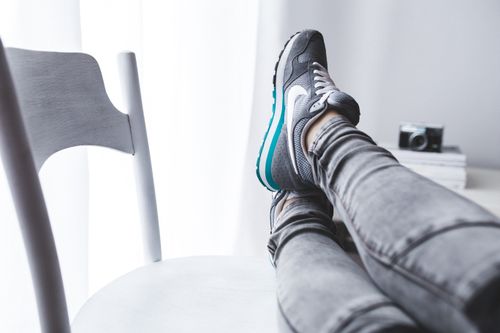 Free A woman lounging with her feet up on a chair, showcasing grey sneakers. Stock Photo