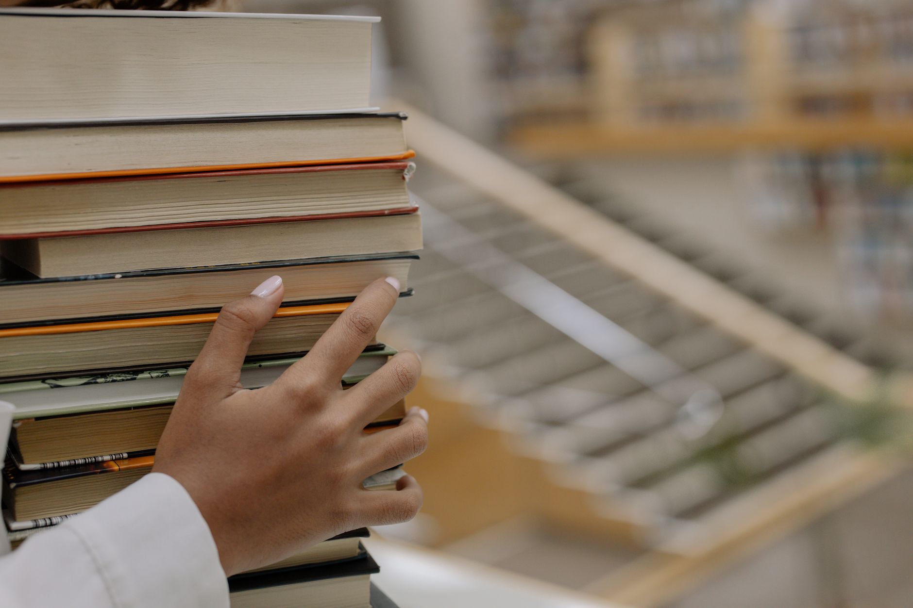 A hand holding a stack of books with bookshelves blurred in the background, depicting knowledge and learning.