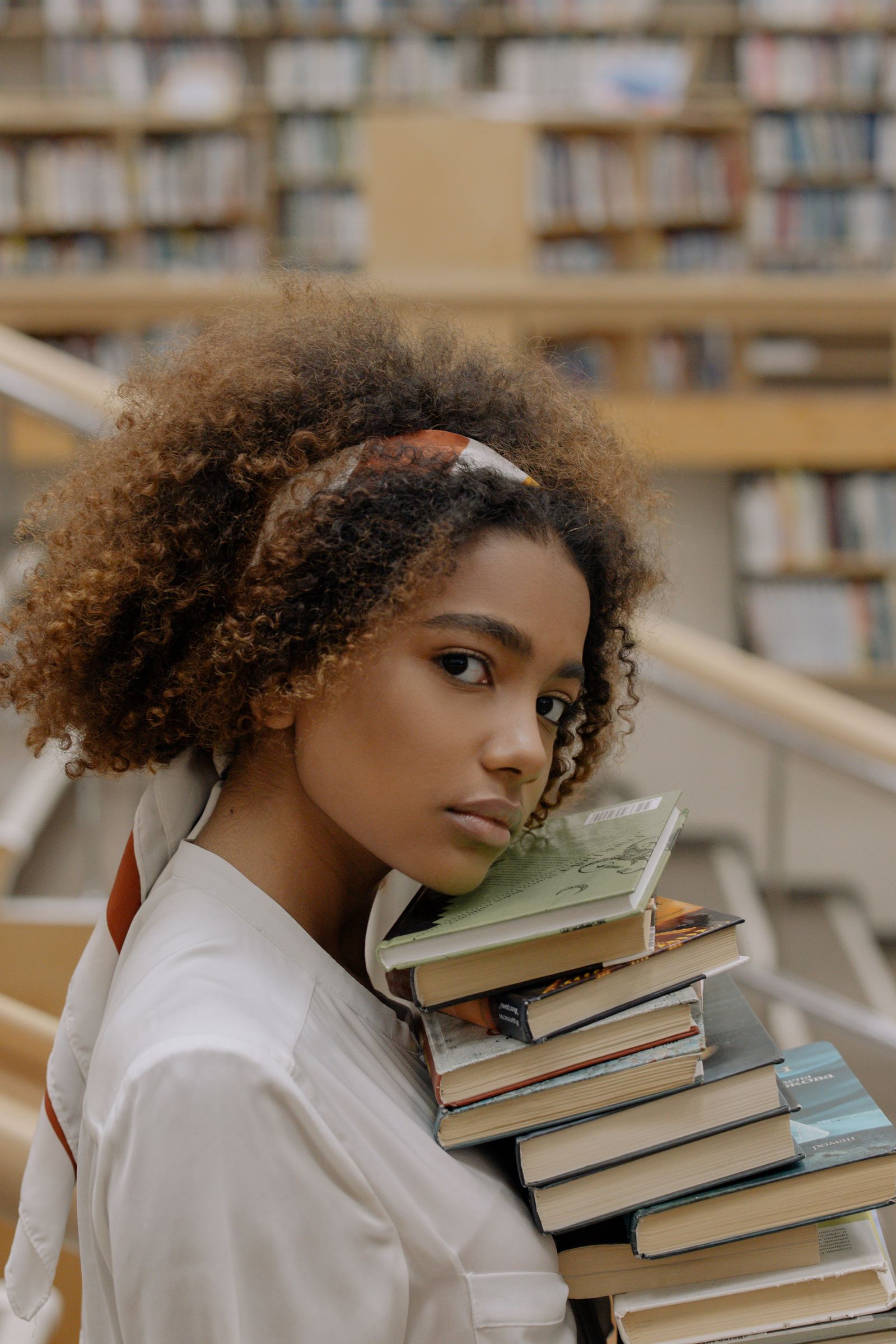 Black reader carrying a stack of books in a library