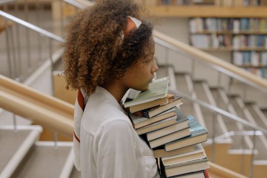African American woman carrying a stack of books in a library, focusing on education.