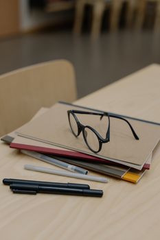 A wooden desk with stacked notebooks, pens, and eyeglasses in a neat arrangement.