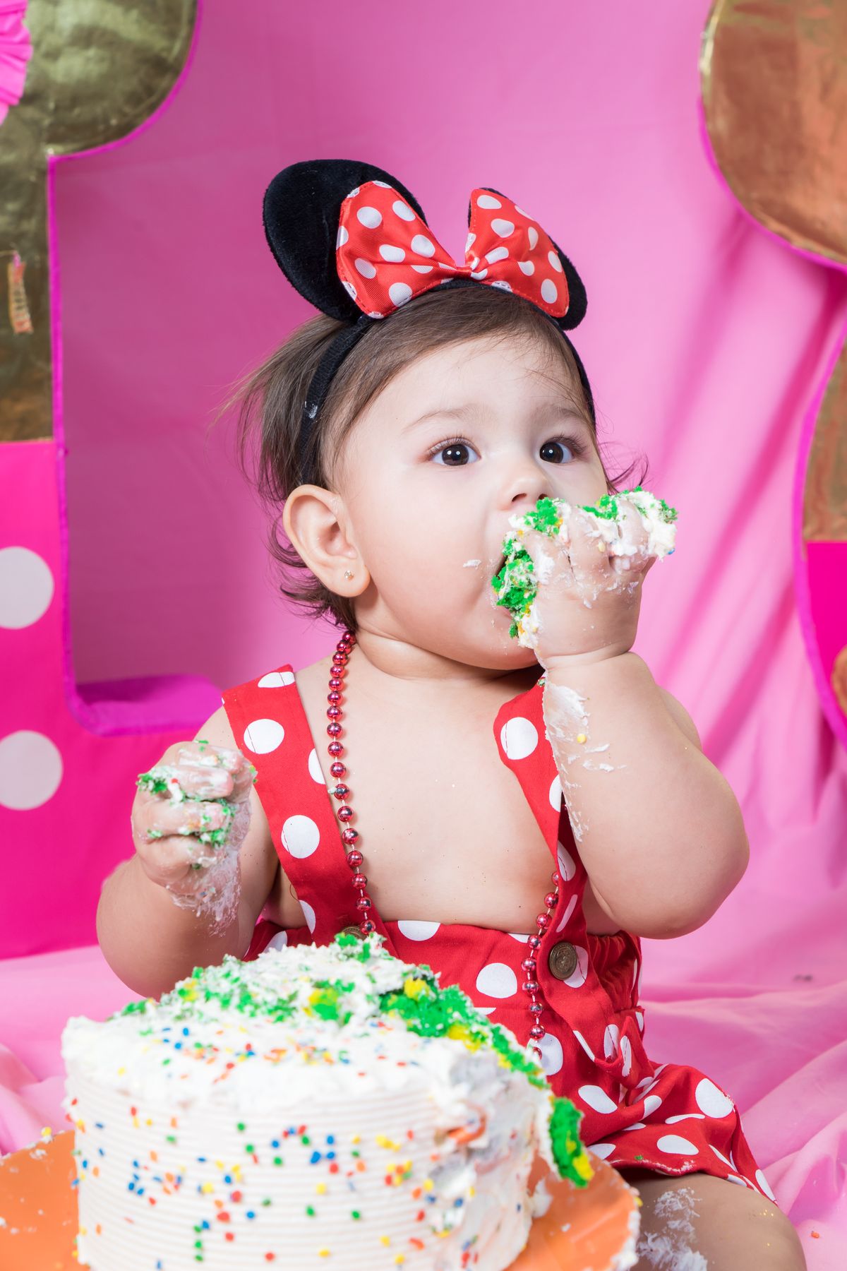 Baby eating cake with frosting on her face at a first birthday smash cake party