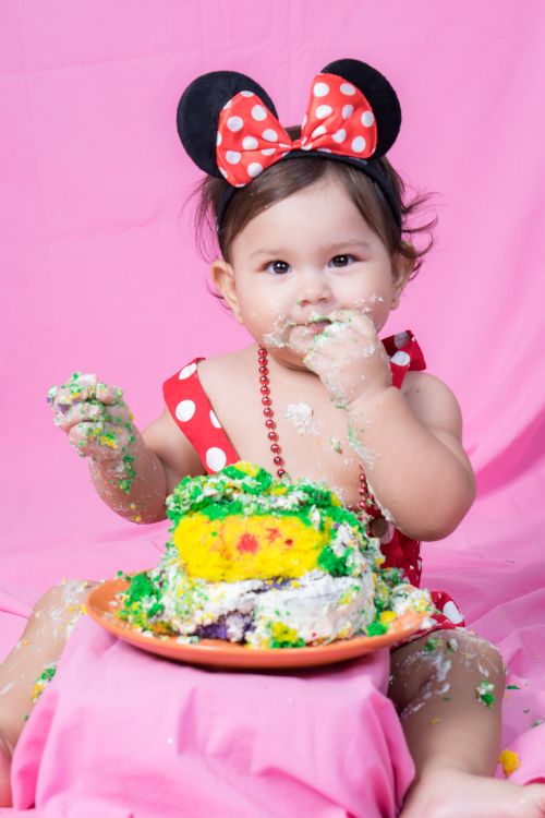 Free Cute baby with mouse ears enjoying a fun cake smash with colorful icing mess. Stock Photo