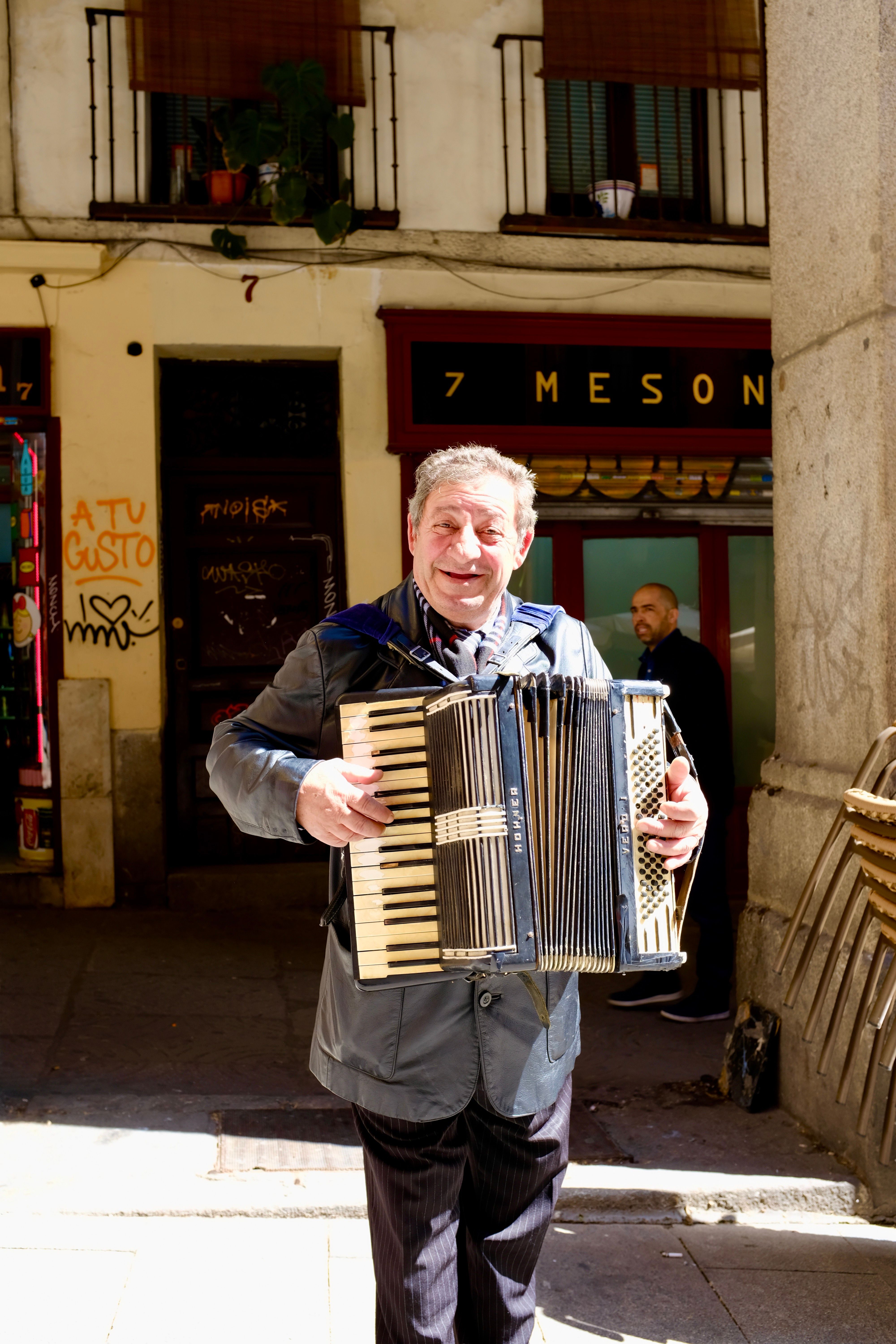 Smiling elderly man plays accordion in a lively Madrid street scene.