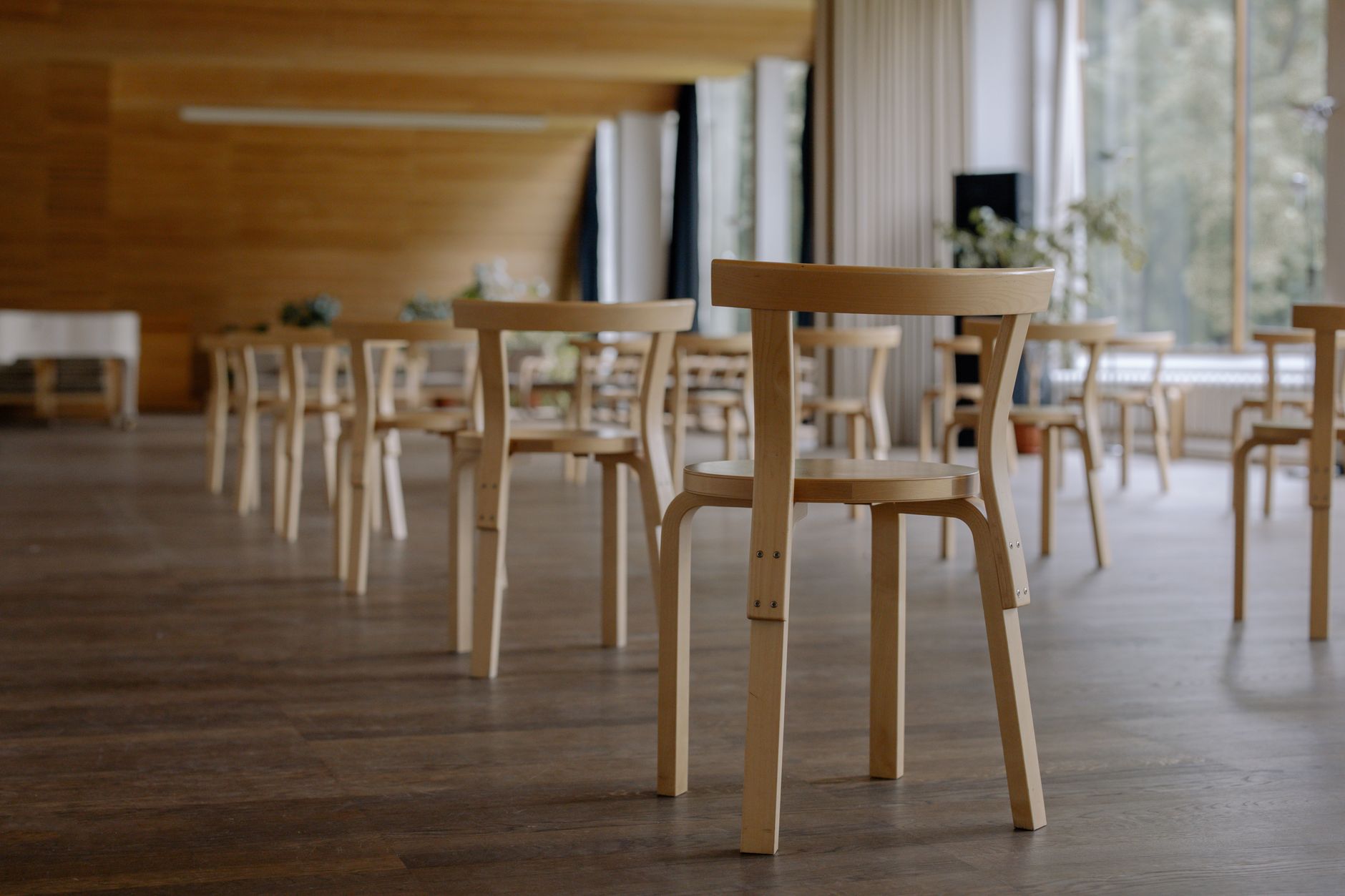 An empty conference hall featuring contemporary wooden chairs and natural lighting.