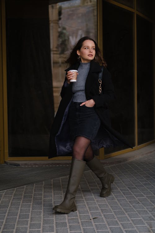 Female with paper cup of coffee on street near buildings