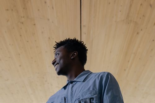 Free Portrait of a smiling young man in a blue shirt looking away, captured indoors. Stock Photo