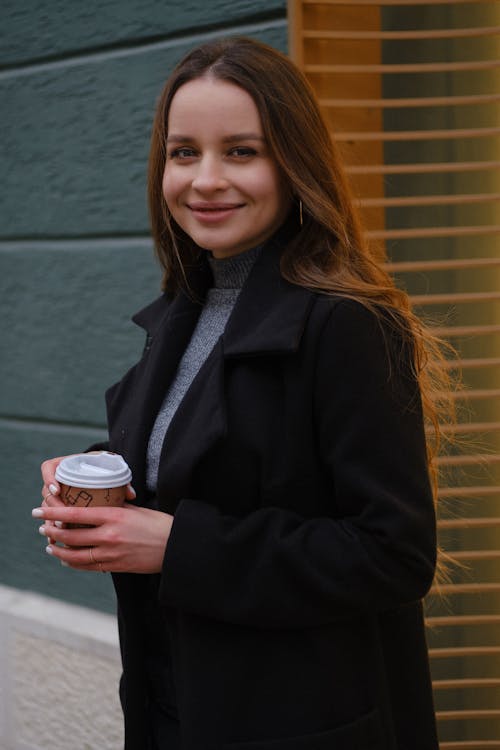 Free Smiling woman with coffee cup standing near brick wall outdoors Stock Photo