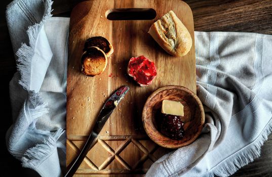 A top view of a rustic breakfast setup with bread, butter, and jam on a wooden board.