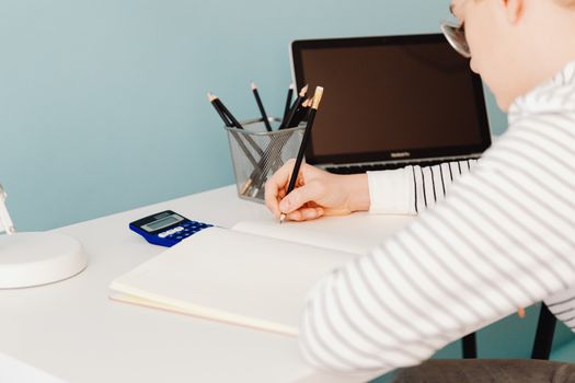 Young adult writing with pencils at a desk with laptop and calculator, perfect for study and work themes.