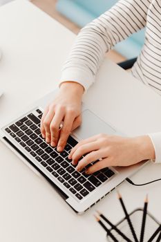 Close-up of hands typing on laptop in a bright, modern workspace.