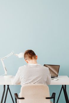 Teen boy studying at a desk with laptop and lamp, minimal design.