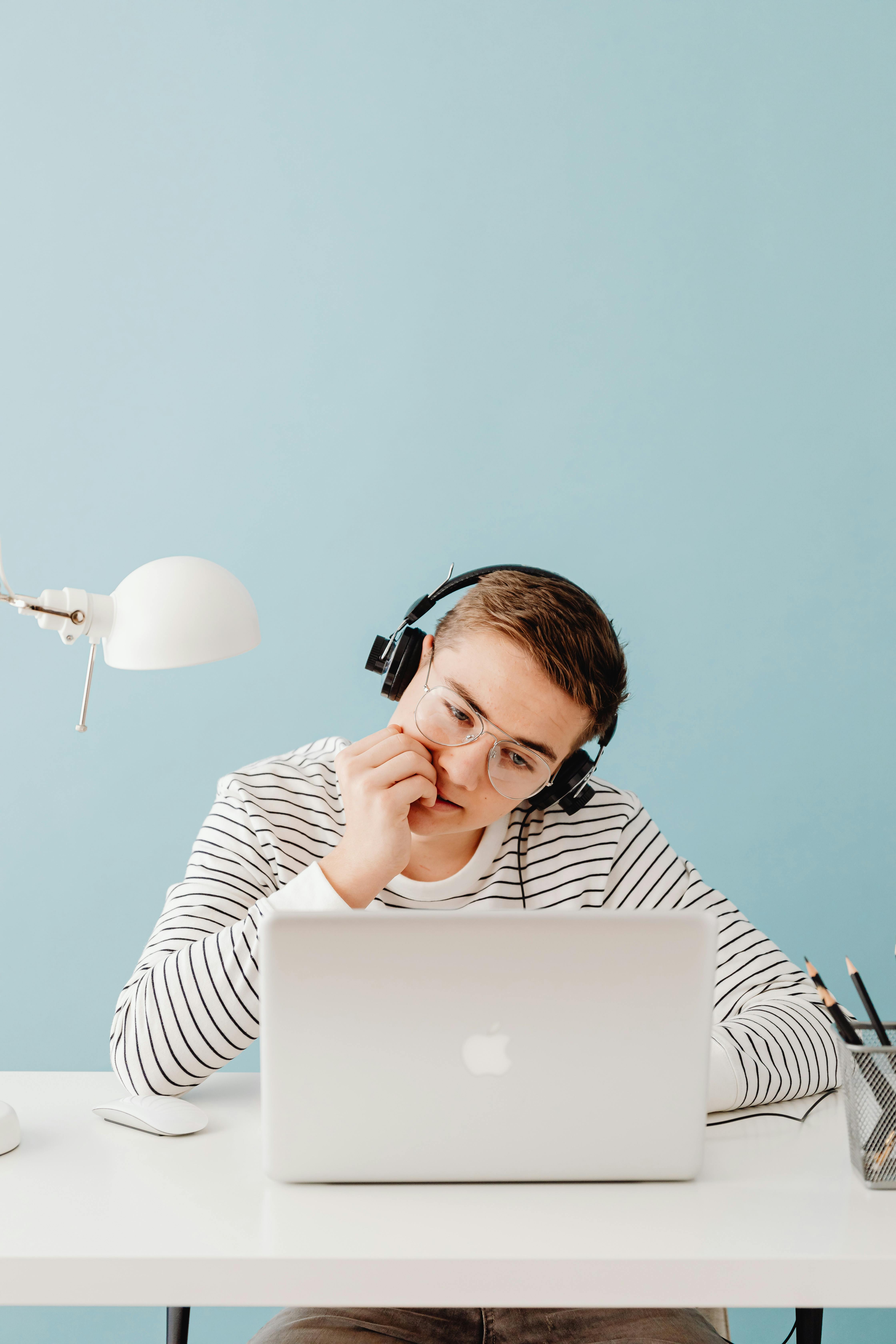 teenage boy sitting behind a desk in headphones using laptop