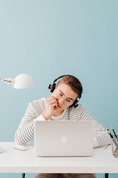 Teenager focused on a laptop while wearing headphones in a minimalist office setting.