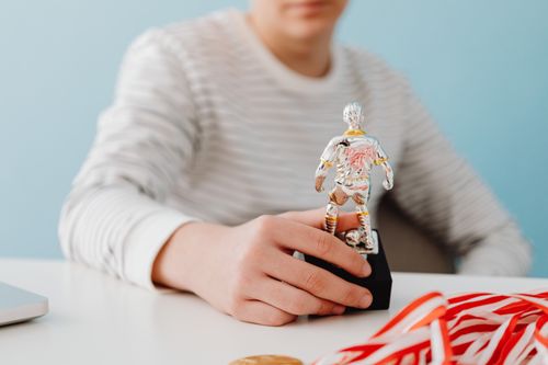 Free Boy holding a silver football player figurine on a desk with ribbons, signifying achievement. Stock Photo