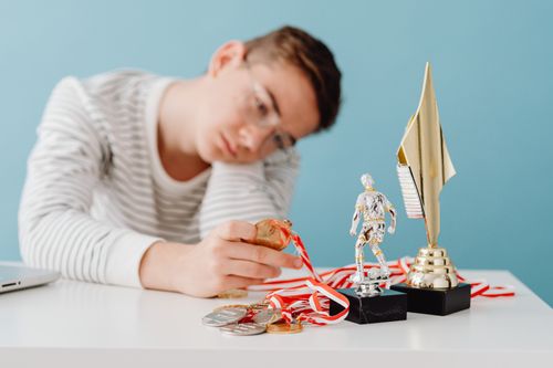 Free A thoughtful teenager sits by a table with various trophies and medals. Stock Photo