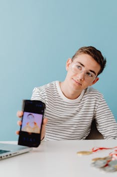 Teen boy showcasing a smartphone with medals beside him on a white desk.