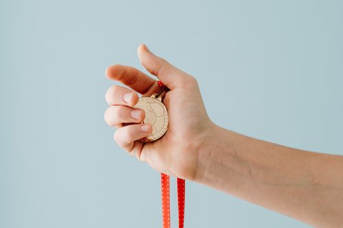 Free A close-up image of a hand holding a gold medal with a red ribbon against a blue background. Stock Photo