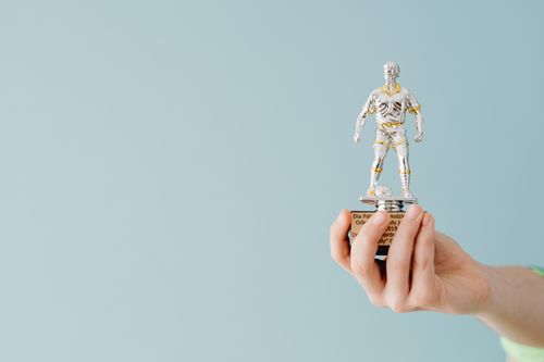 Free A hand holds a soccer trophy against a blue background, symbolizing success and achievement. Stock Photo