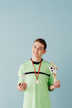 Smiling teen athlete holding trophies and medal against a blue background.