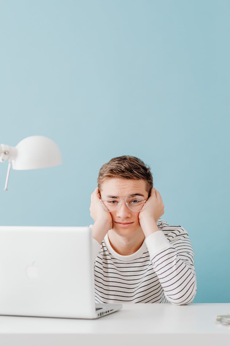 Bored Guy Sitting At Desk Studying On Laptop