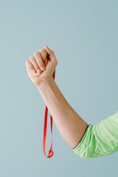 A close-up shot of a hand in a green sleeve holding a red ribbon against a blue background.